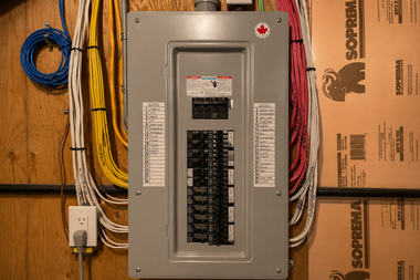 Electrical breaker panel on a wall with colored wiring and cardboard boxes nearby