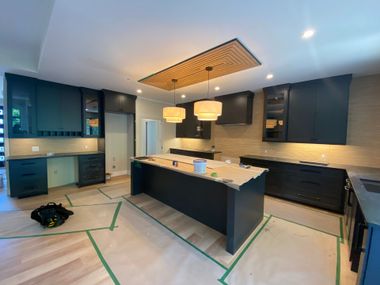 Modern kitchen with dark cabinets, white island, pendant lights, and taped-off floor under renovation