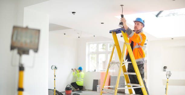 Worker in orange safety vest and blue hard hat repairing ceiling with ladder in a bright room