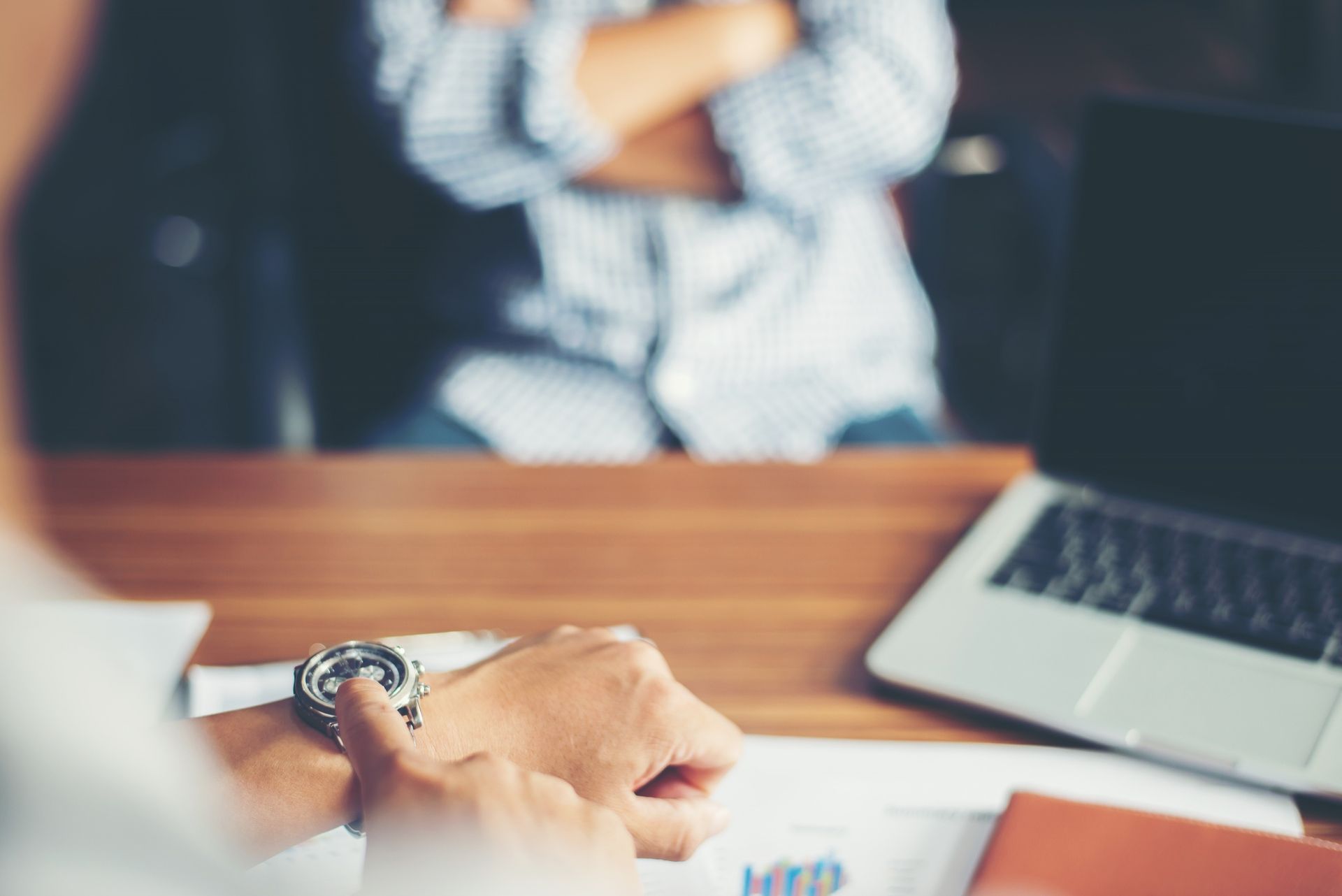 Person looking at their wristwatch during a meeting; laptop and paperwork on the desk.