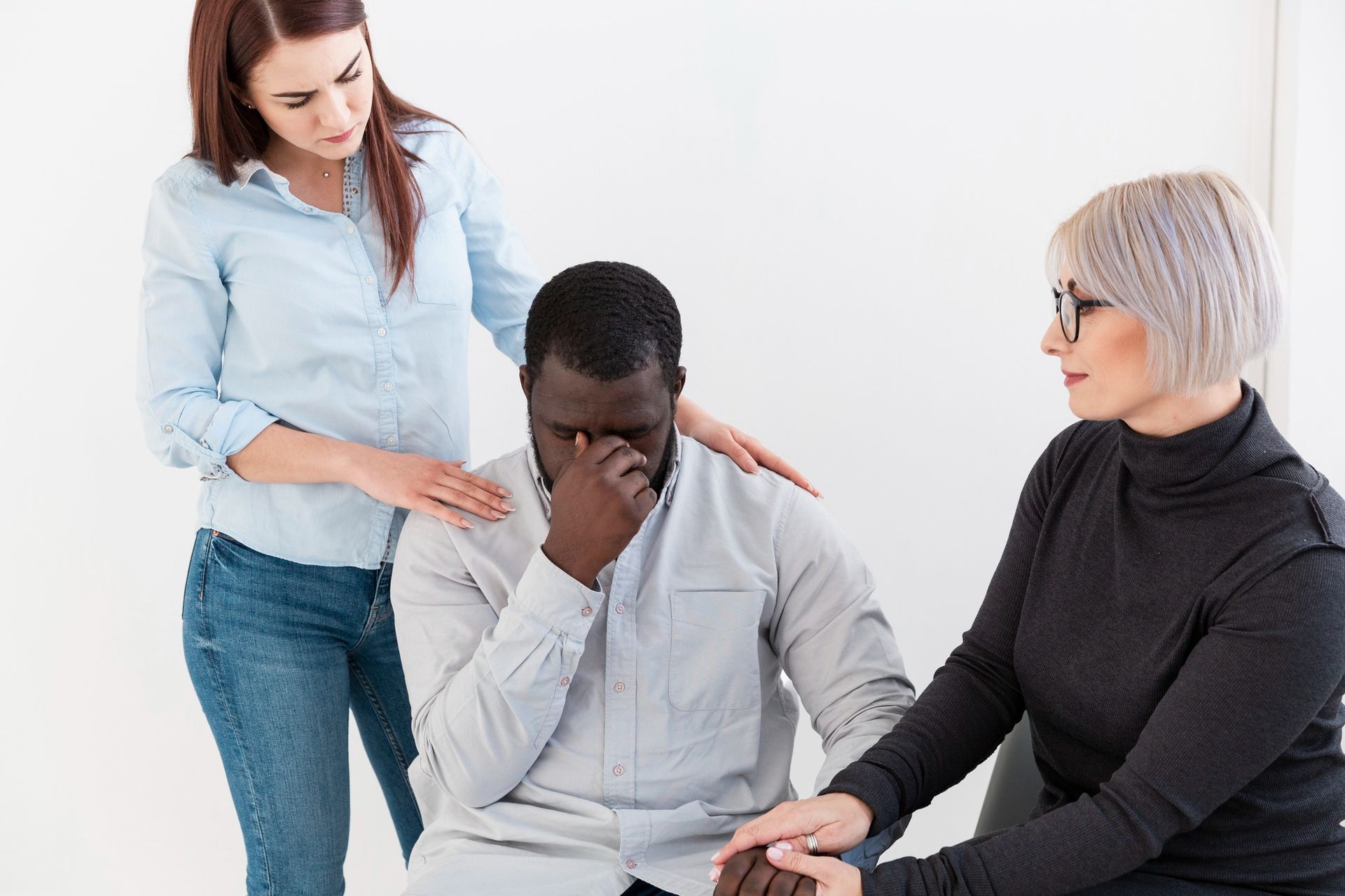 A man is sitting in a chair while two women comfort him.