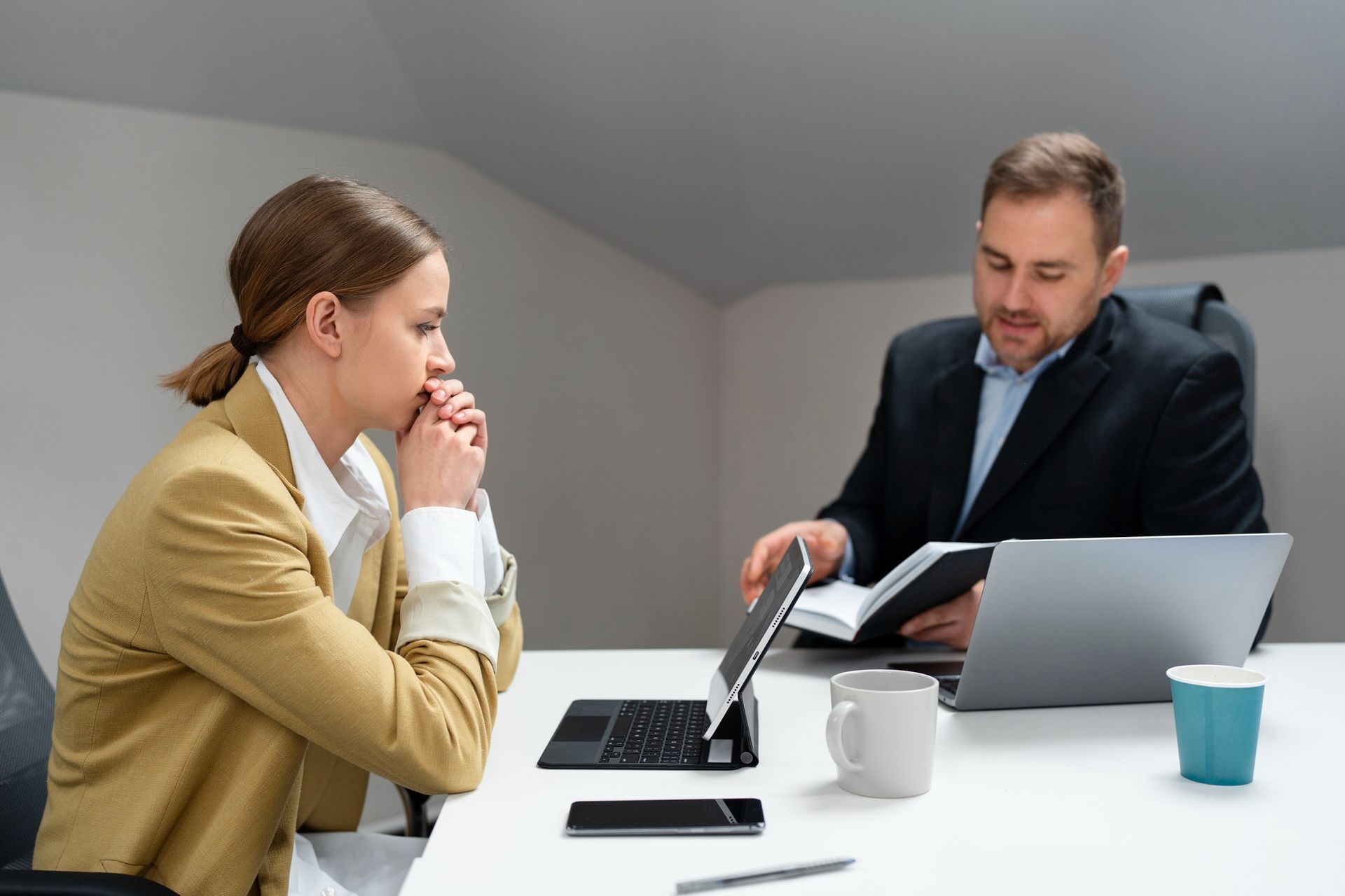 A man and a woman are sitting at a table with laptops.