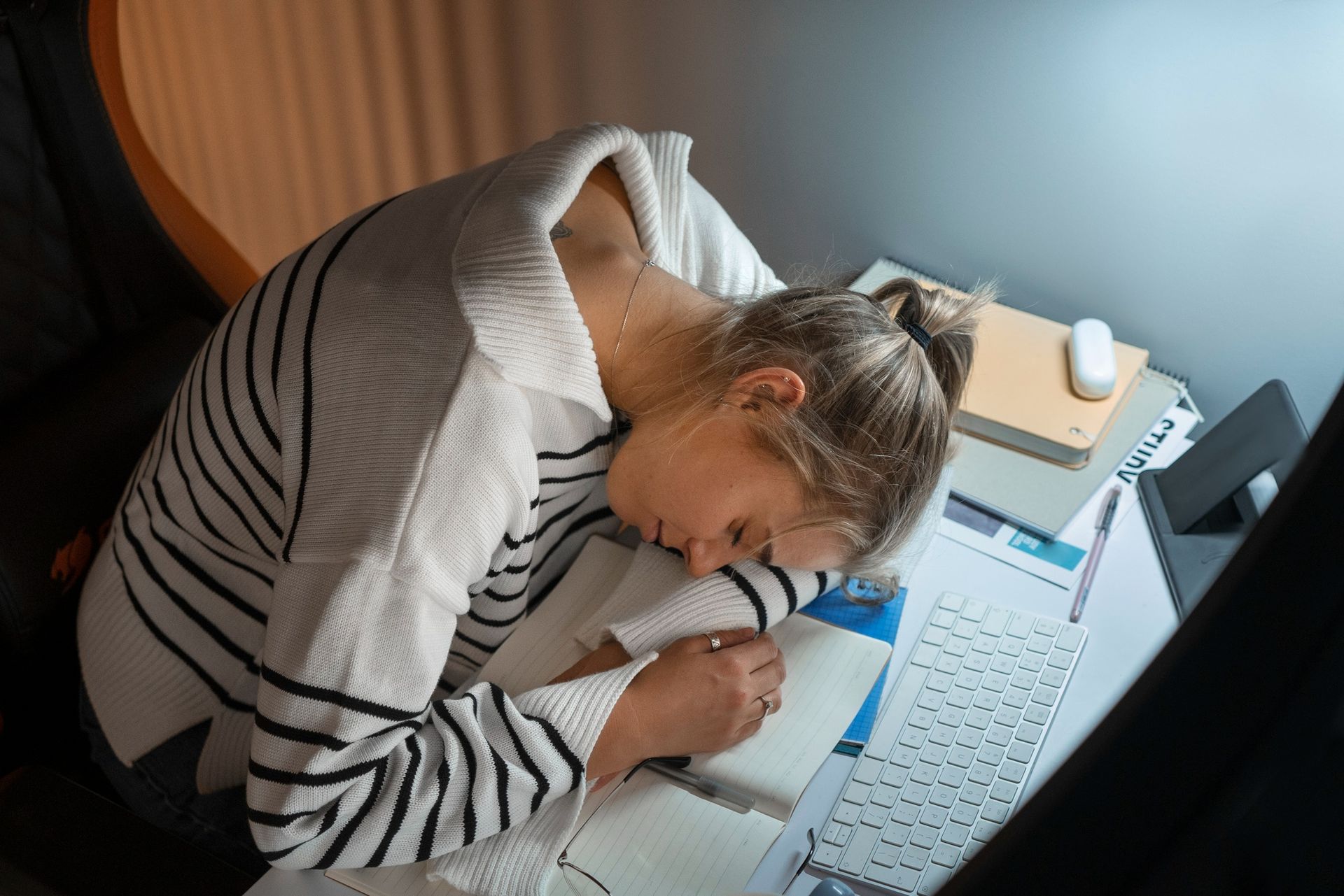 A woman is sleeping at a desk in front of a laptop computer.