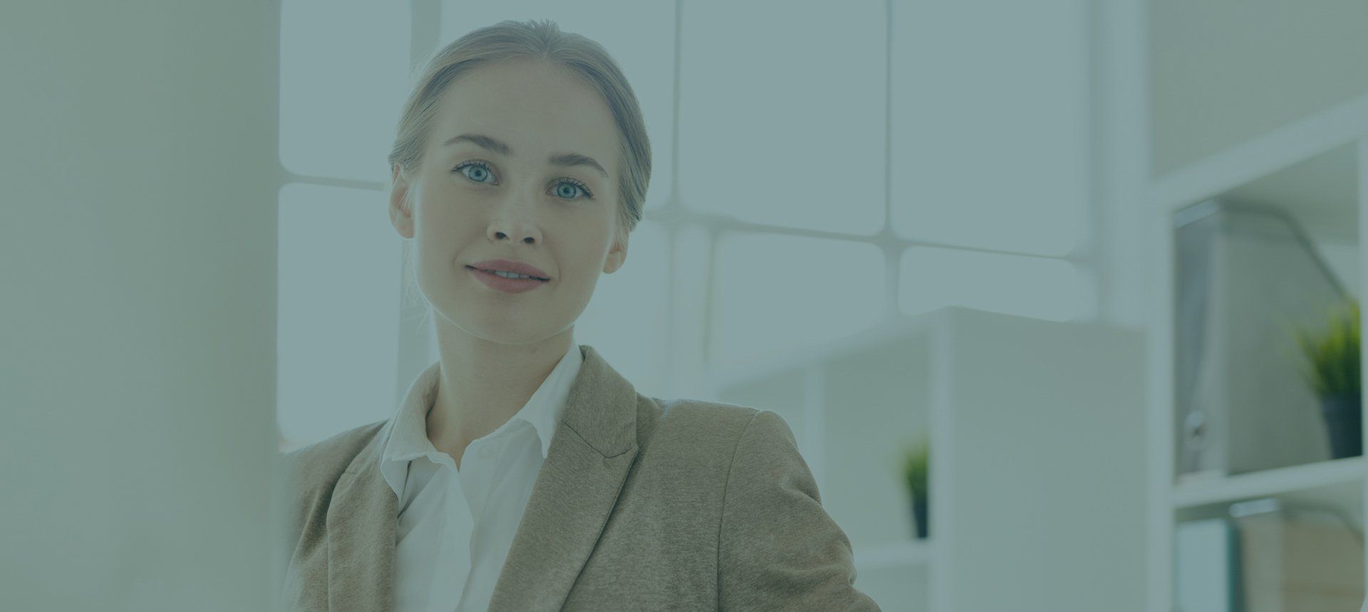 A woman in a suit is standing in an office looking at the camera.
