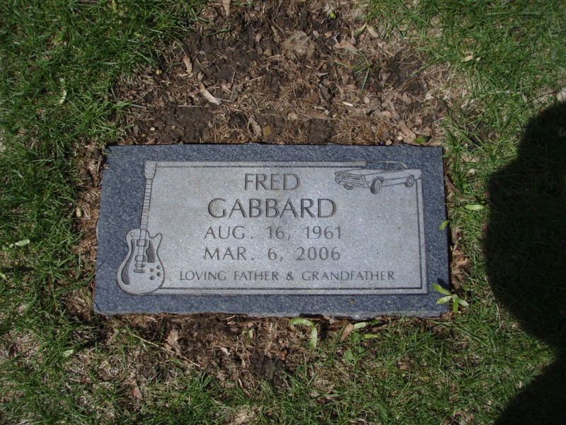 Fred Gabbard's tombstone. Rectangular gray marker with engraved text and guitar icon, set in grass.