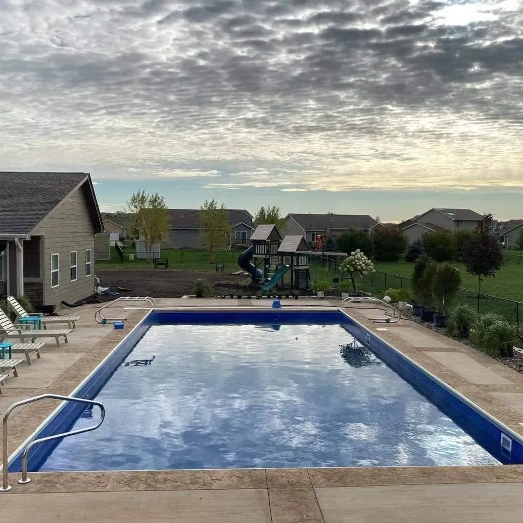 A large swimming pool is in the backyard of a house.