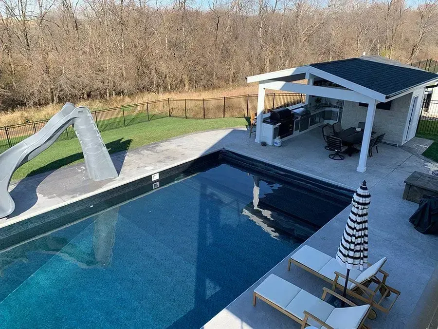 Modern backyard pool built by a custom pool contractor with modern features and a stone deck. 