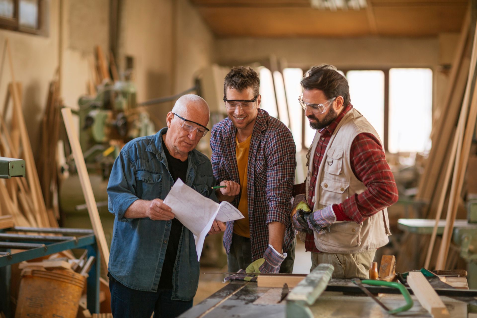 Three men are working in a woodworking shop and looking at a piece of paper.