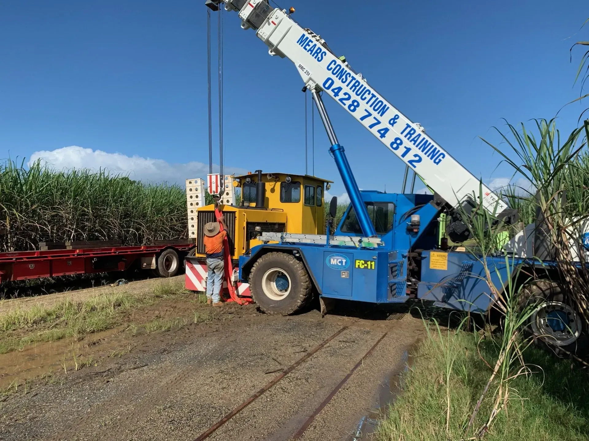 Crane Lifting A Yellow Machine Near Sugarcane Fields — Mears Construction & Training Pty Ltd in South Johnstone, QLD