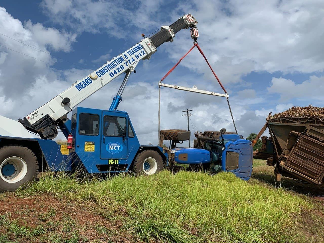 A Blue Crane Lifting A Metal Frame Over Machinery In A Field — Mears Construction & Training Pty Ltd in South Johnstone, QLD