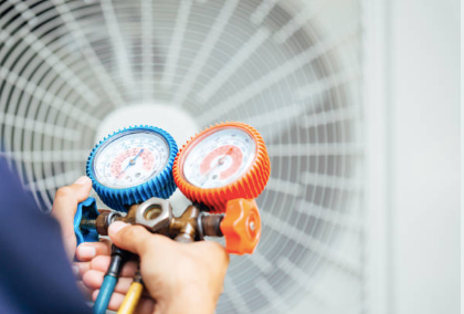 A person is holding two gauges in front of an air conditioner.