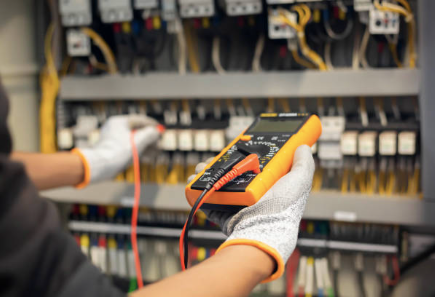 A person is holding a multimeter in their hand in front of a electrical panel.