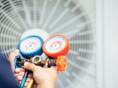 A person is holding two gauges in front of an air conditioner.