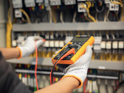 A person is holding a multimeter in their hand in front of a electrical panel.