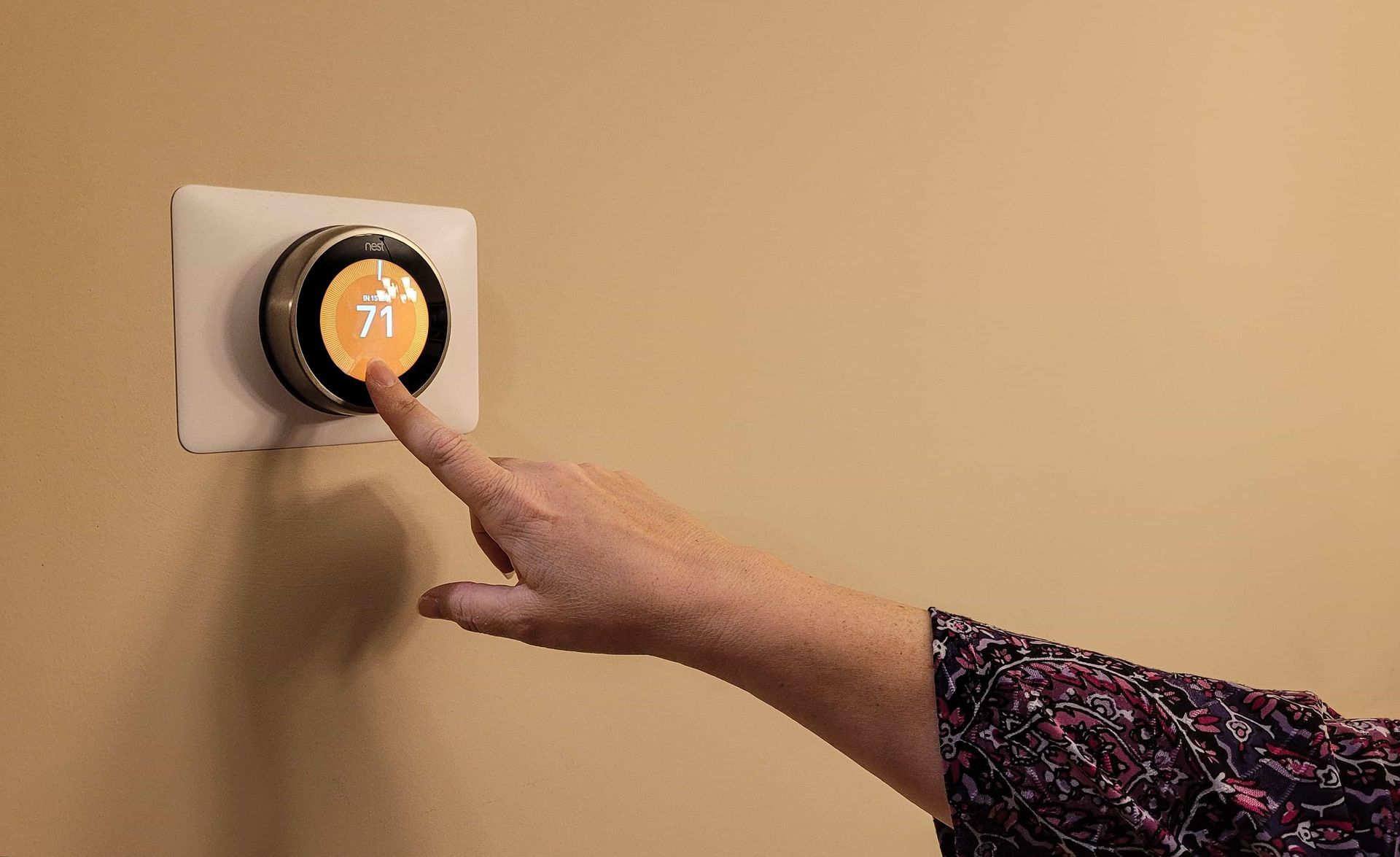 A person is pressing a button on a thermostat on a wall.