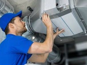 A man is working on a ventilation system in a building.