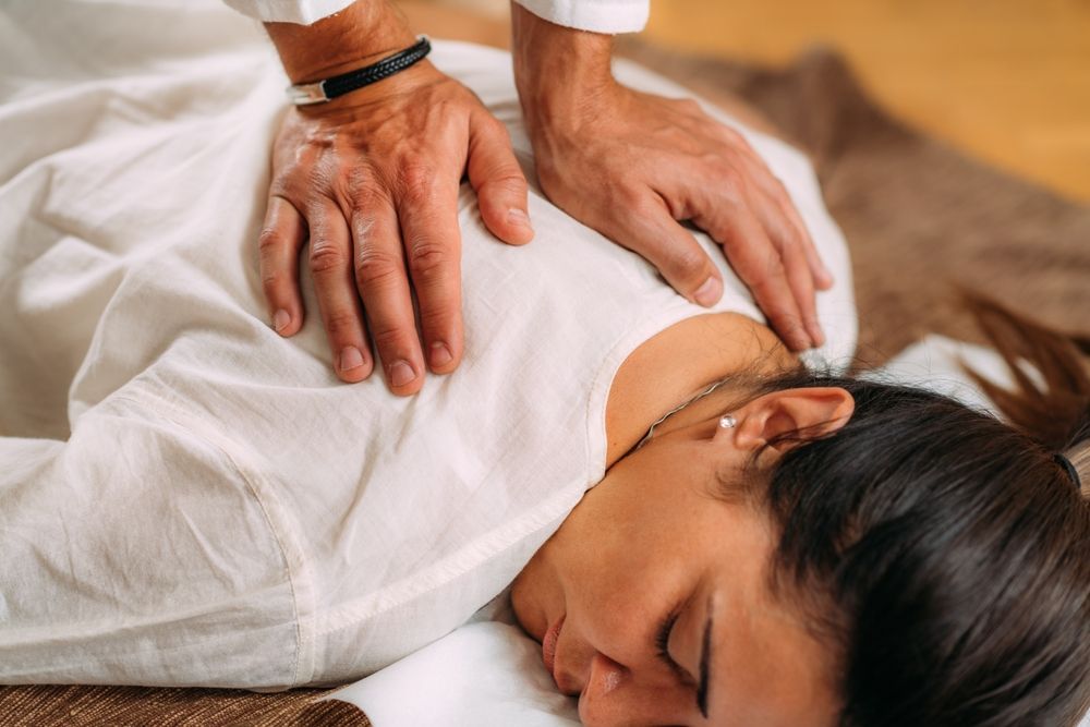 Hands giving a back massage to a woman lying face down on a table, eyes closed.