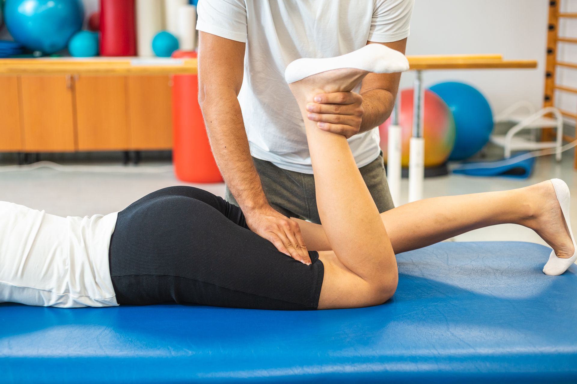 A man is stretching a woman 's leg on a blue mat.