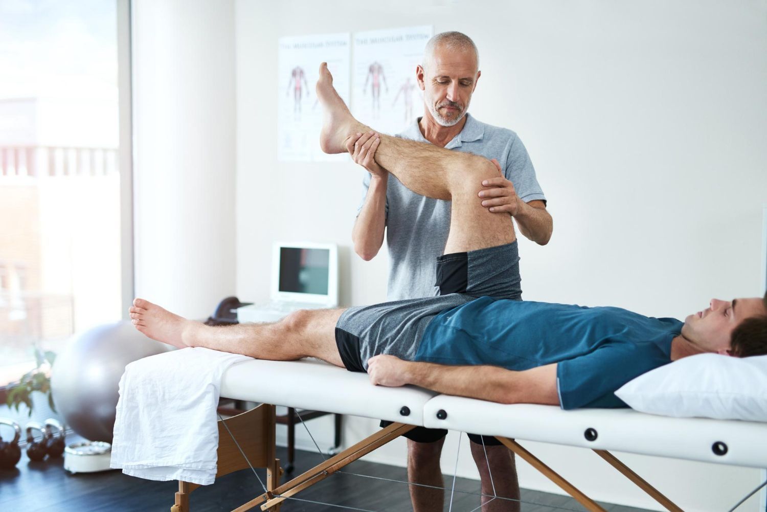 A man is laying on a table getting a leg massage from a doctor.