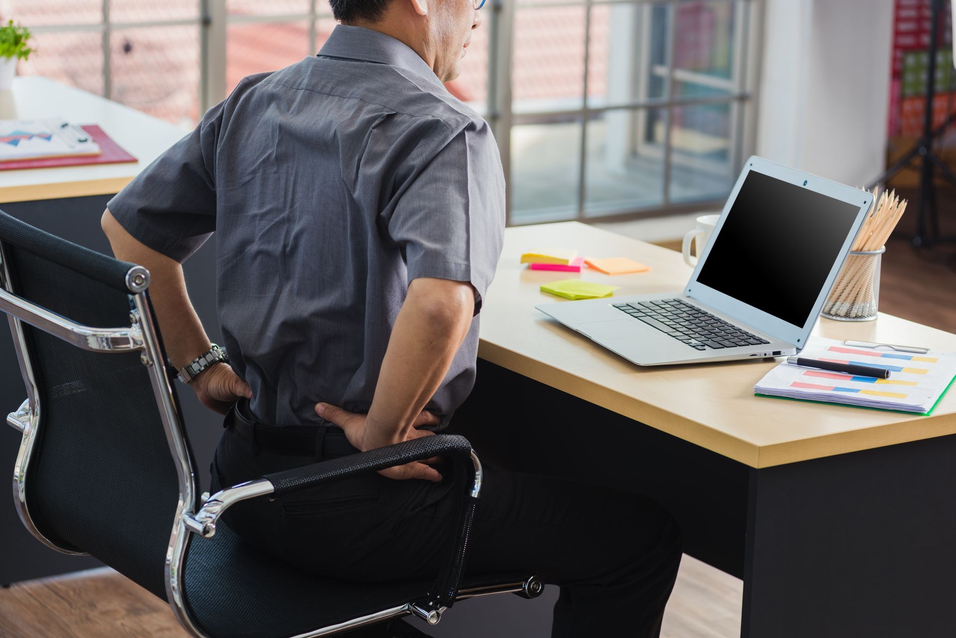 A man is sitting in an office chair with his hands on his back.