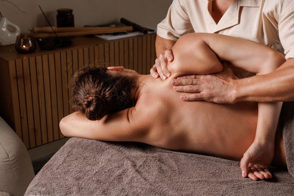 Massage therapist applying back massage to a person lying face down on a table in a warm spa setting