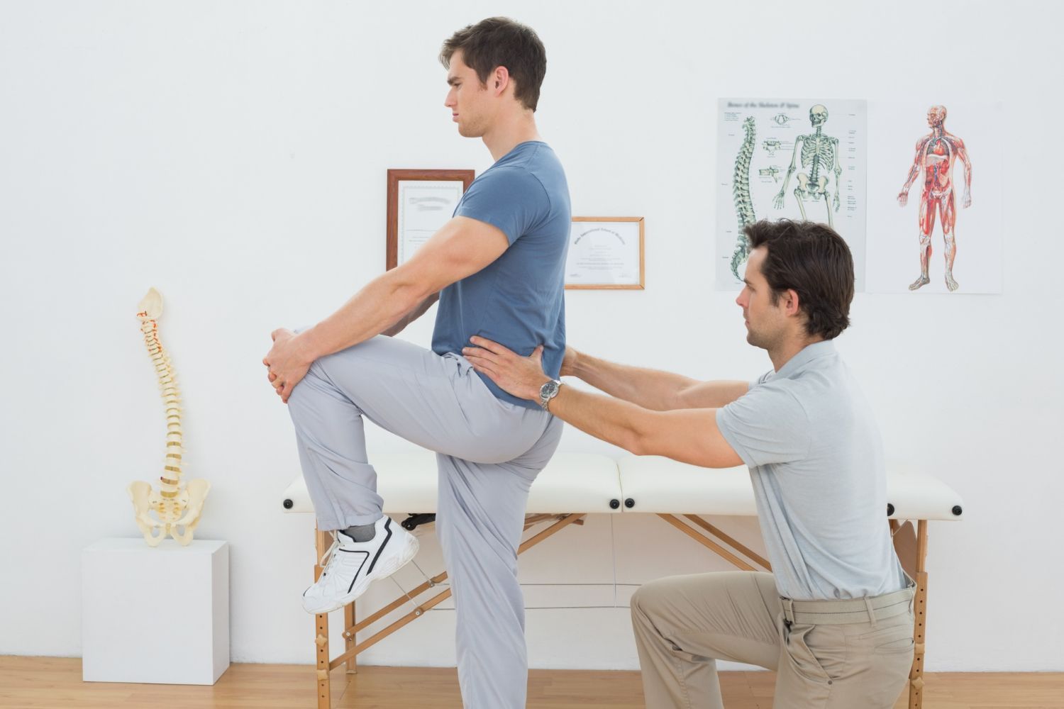 A man is kneeling down to help another man stretch his legs.