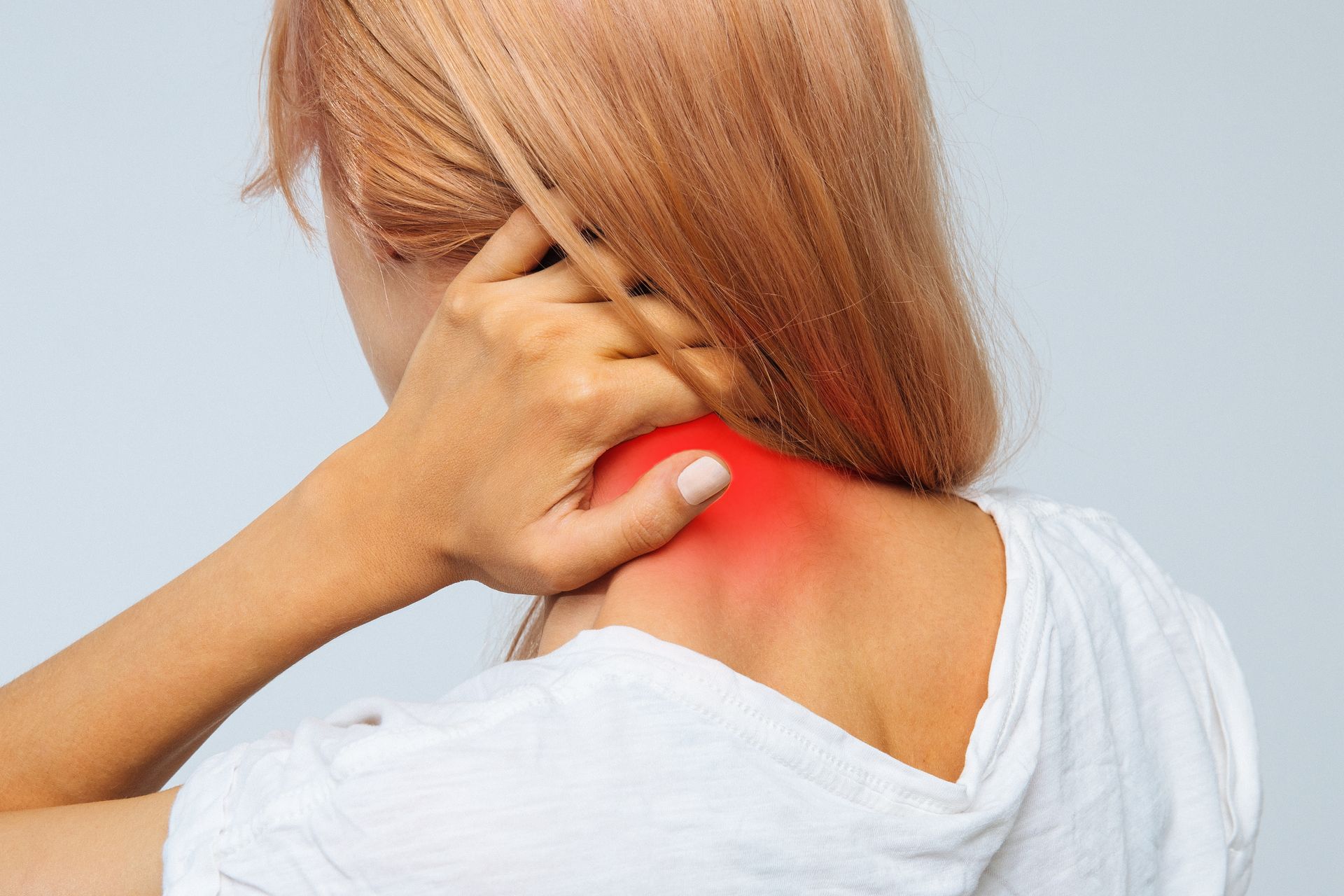 A woman is holding her neck in pain and has a red spot on her neck.