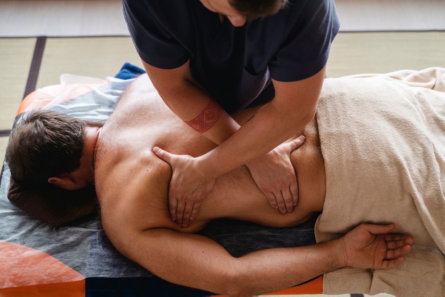 A man is laying on a bed getting a massage from a massage therapist.