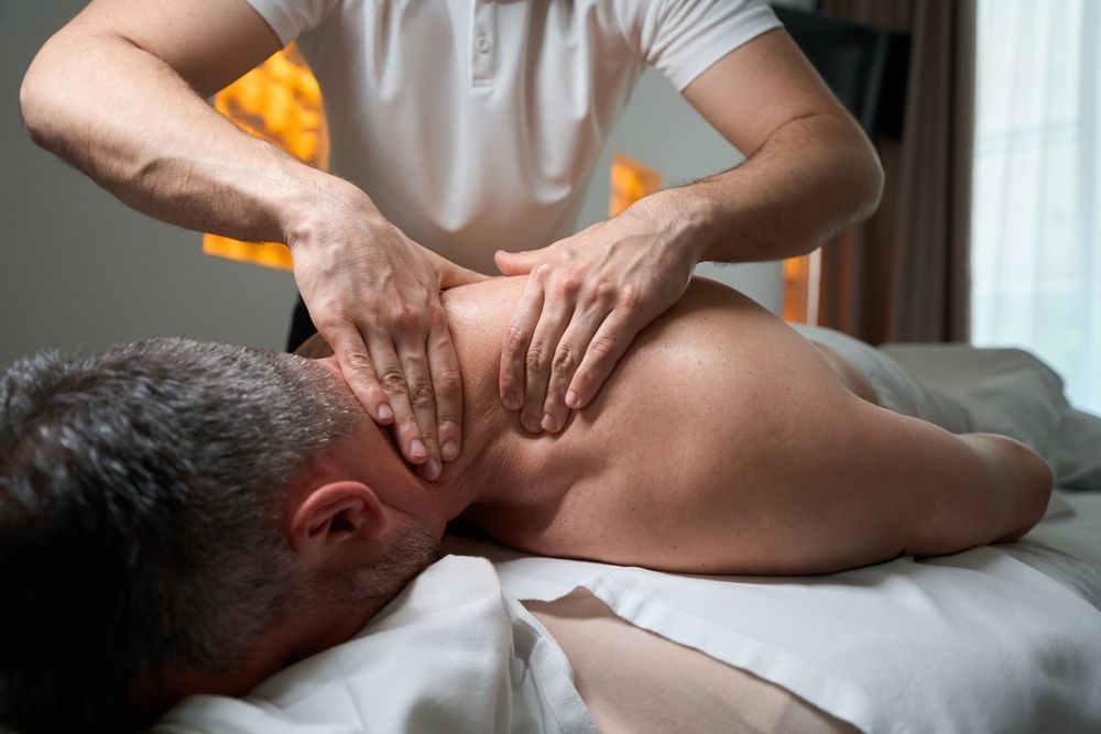 Massage therapist kneading a client’s back on a treatment table in a spa room