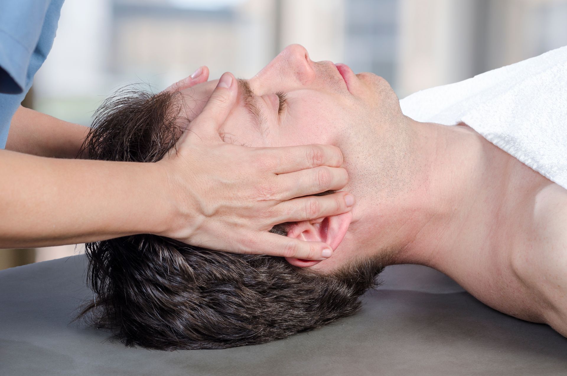 Man receiving head massage, hands on forehead and temples, relaxing on a table, white towel.
