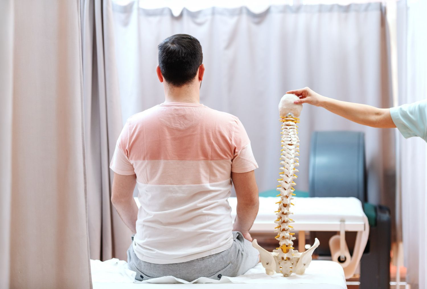 Person seated on a table while a hand holds a hanging spine model beside them