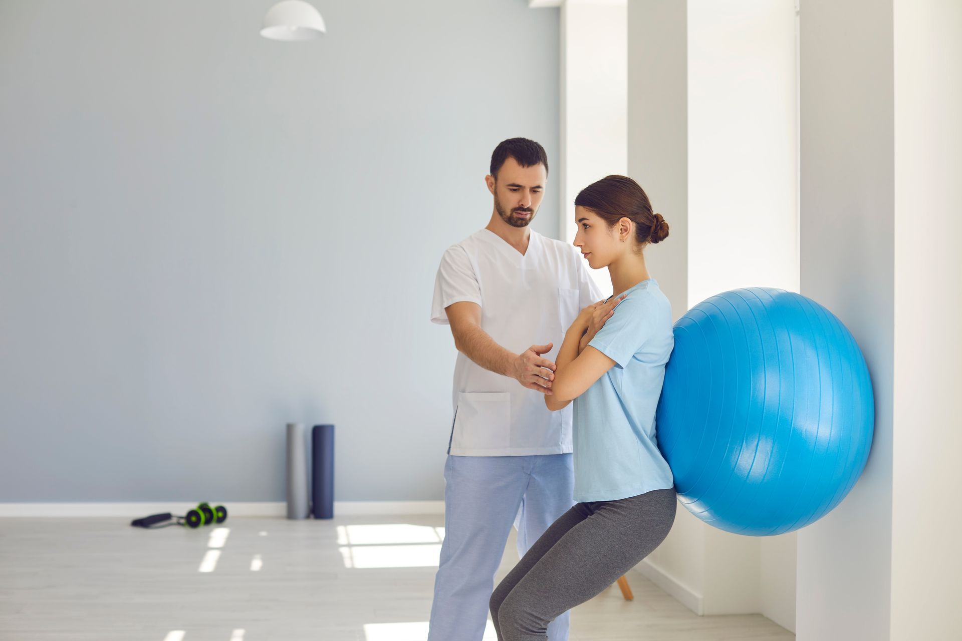 A man is helping a woman squat with a blue exercise ball.