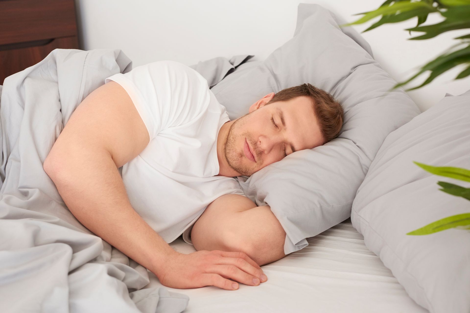 Man sleeping in bed, wearing a white shirt, with gray bedding.