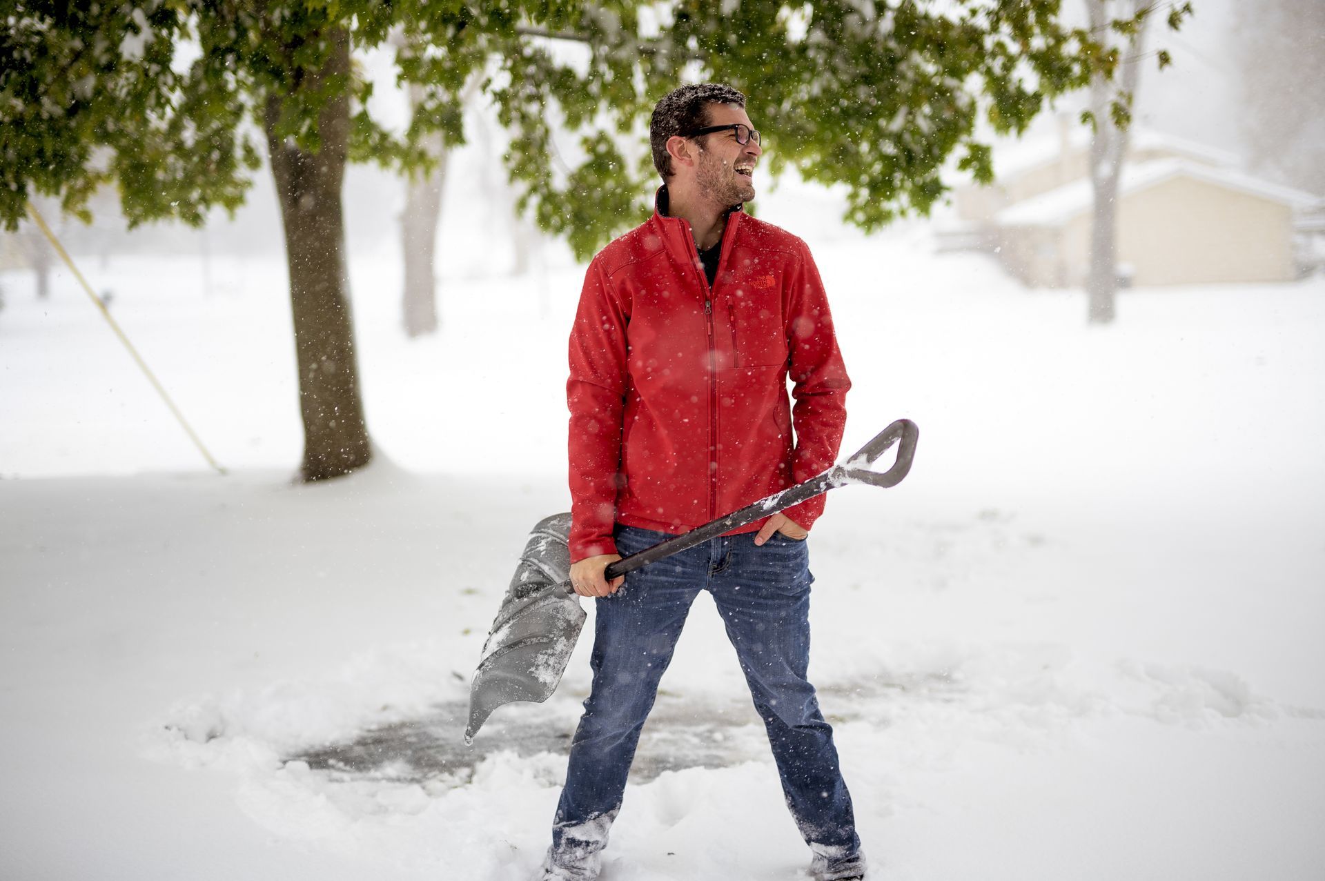 Man in red jacket smiles in the snow, holding a shovel.