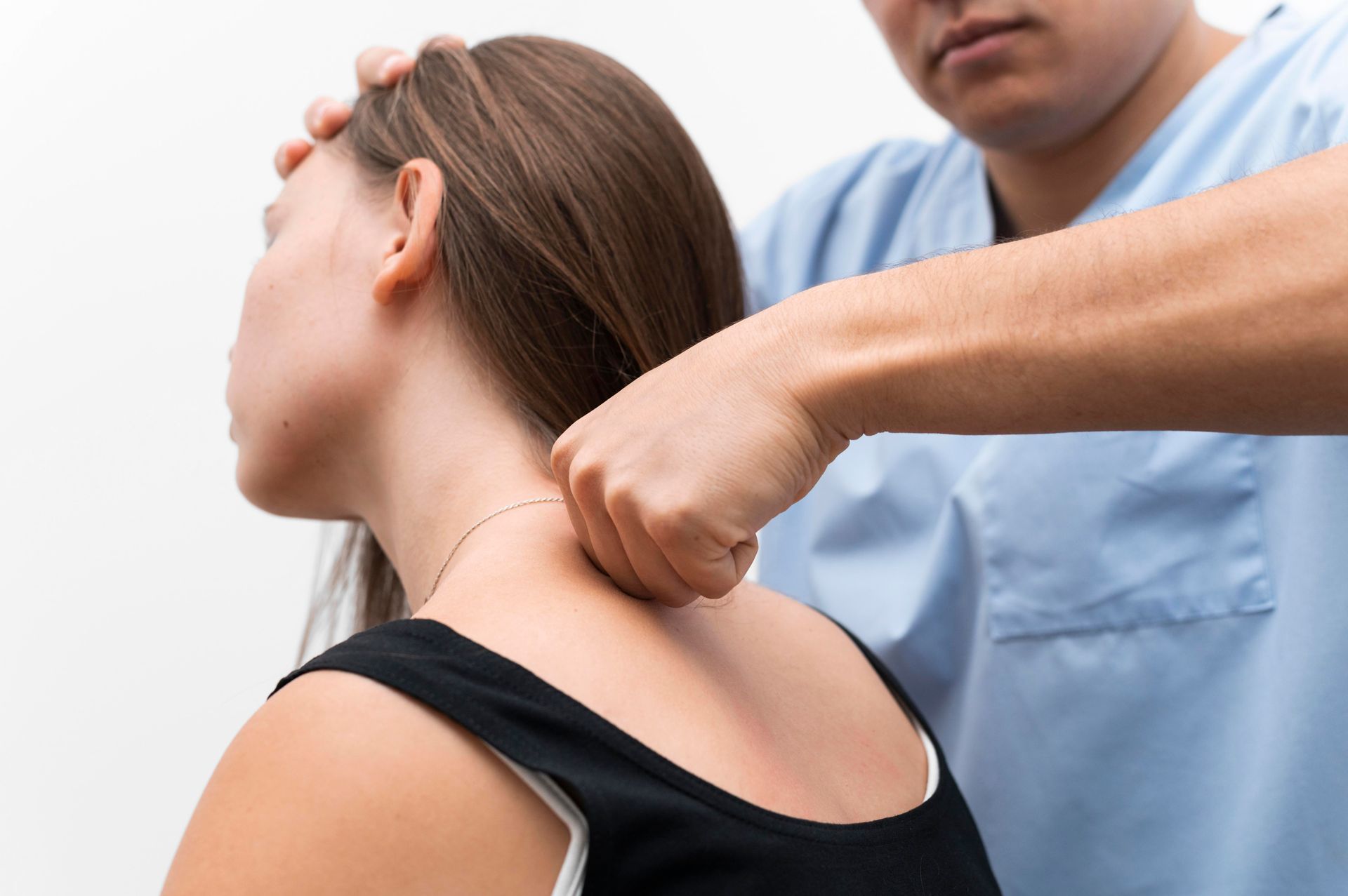 Chiropractor adjusting a woman's neck. White background. The woman is wearing black and the chiropractor is in blue.