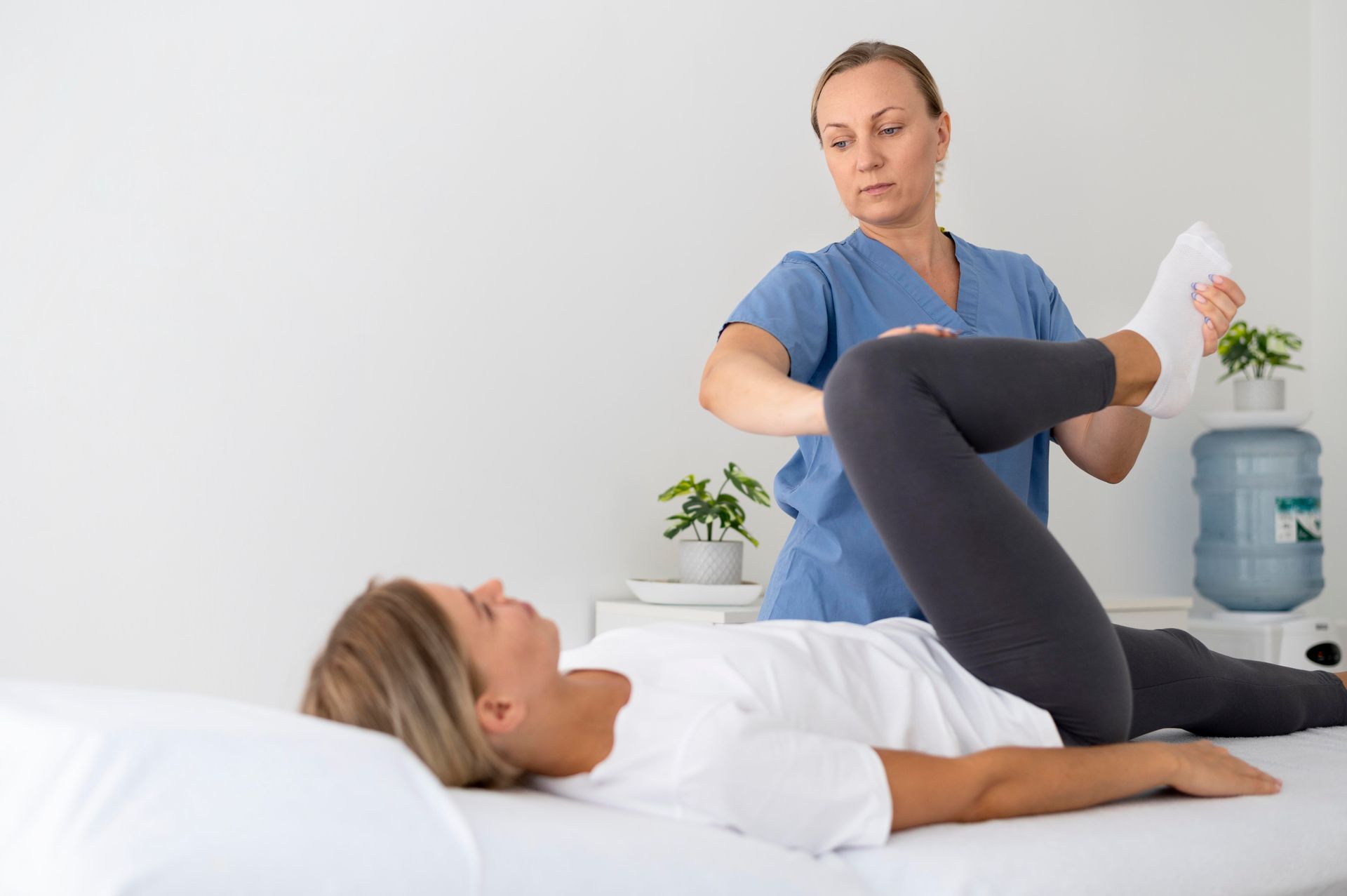 A woman is laying on a bed while a nurse stretches her leg.