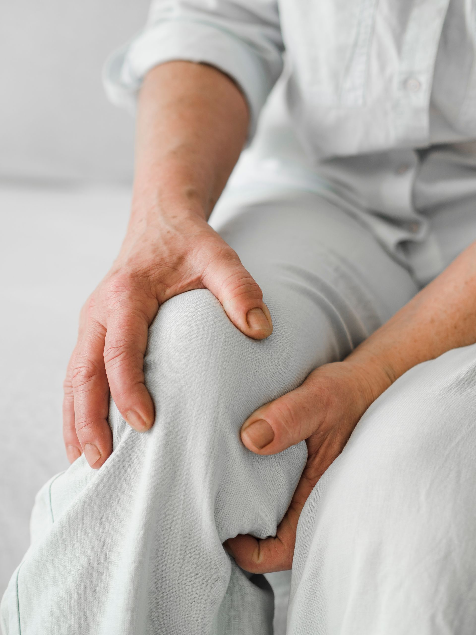 A woman is sitting on a bed holding her knee in pain.