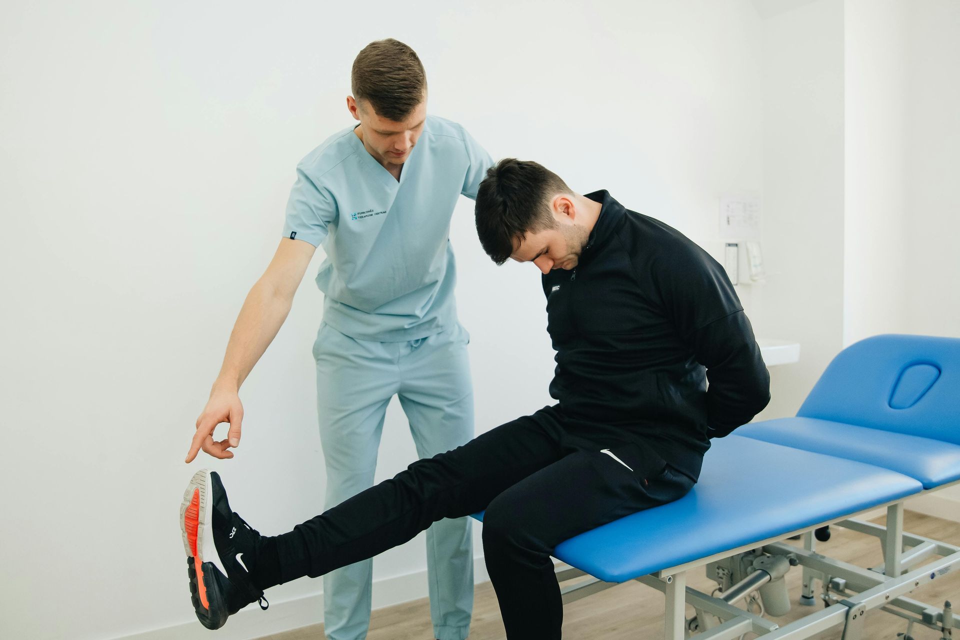 A man is sitting on a blue table while a doctor examines his leg.