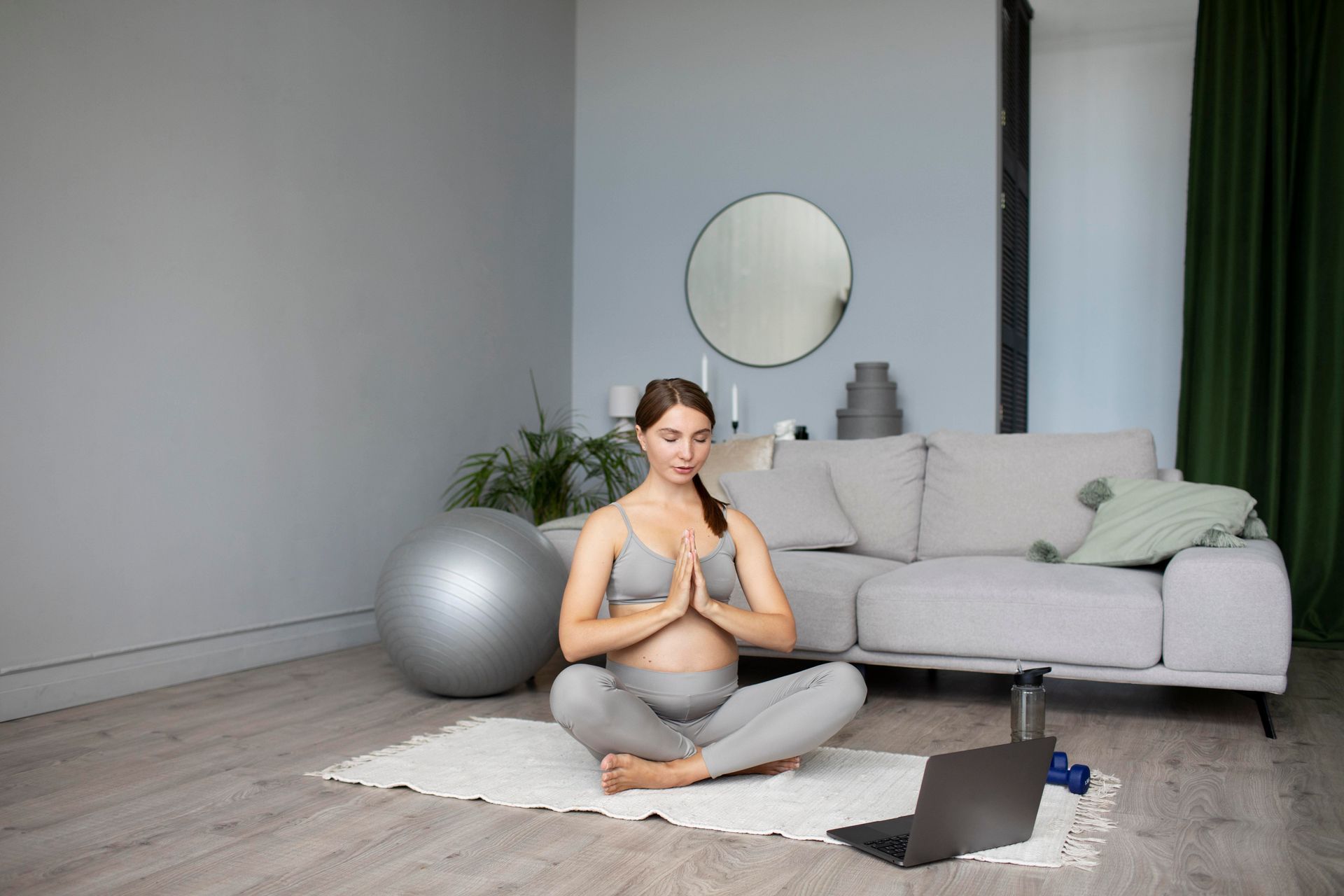 A pregnant woman is sitting on a yoga mat in a living room.