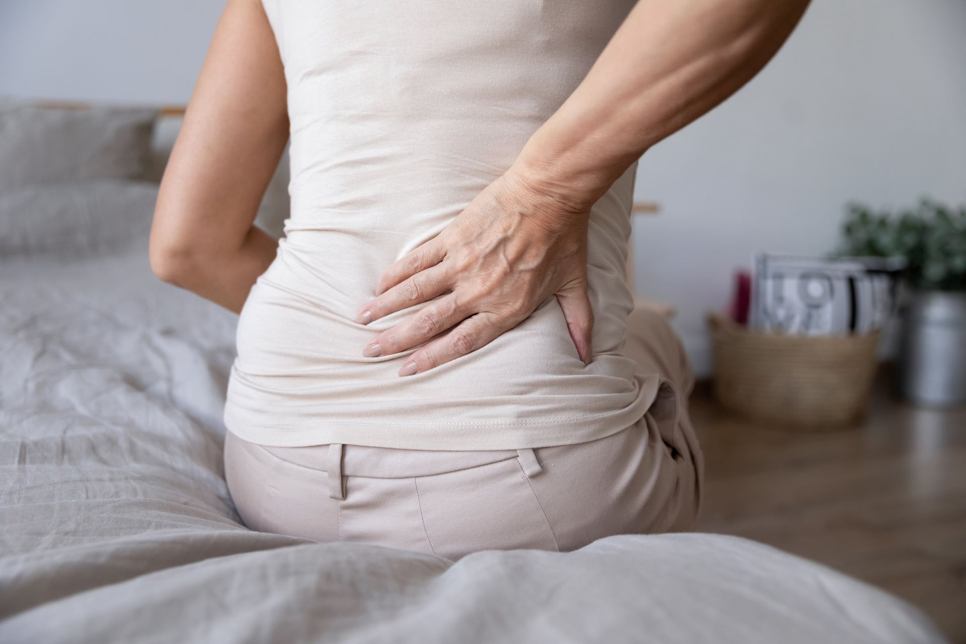 A woman is sitting on a bed holding her back in pain.