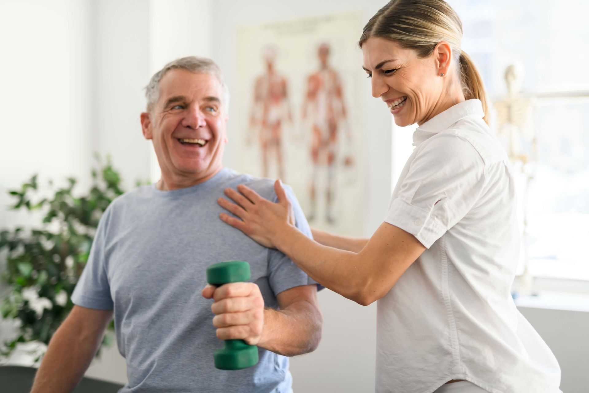 A woman is helping an older man lift a green dumbbell.