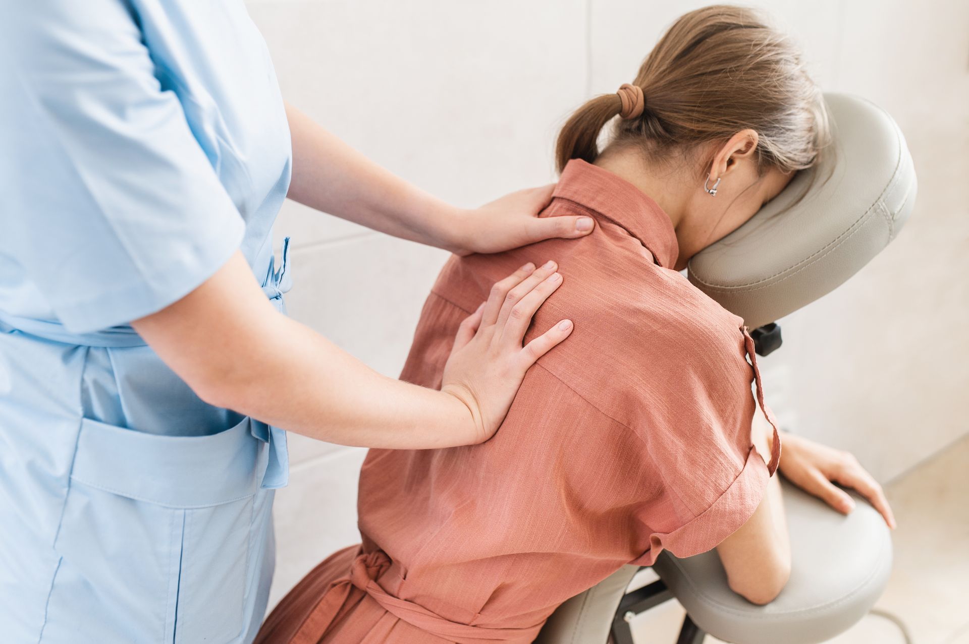 A woman is sitting in a chair getting a massage from a nurse.