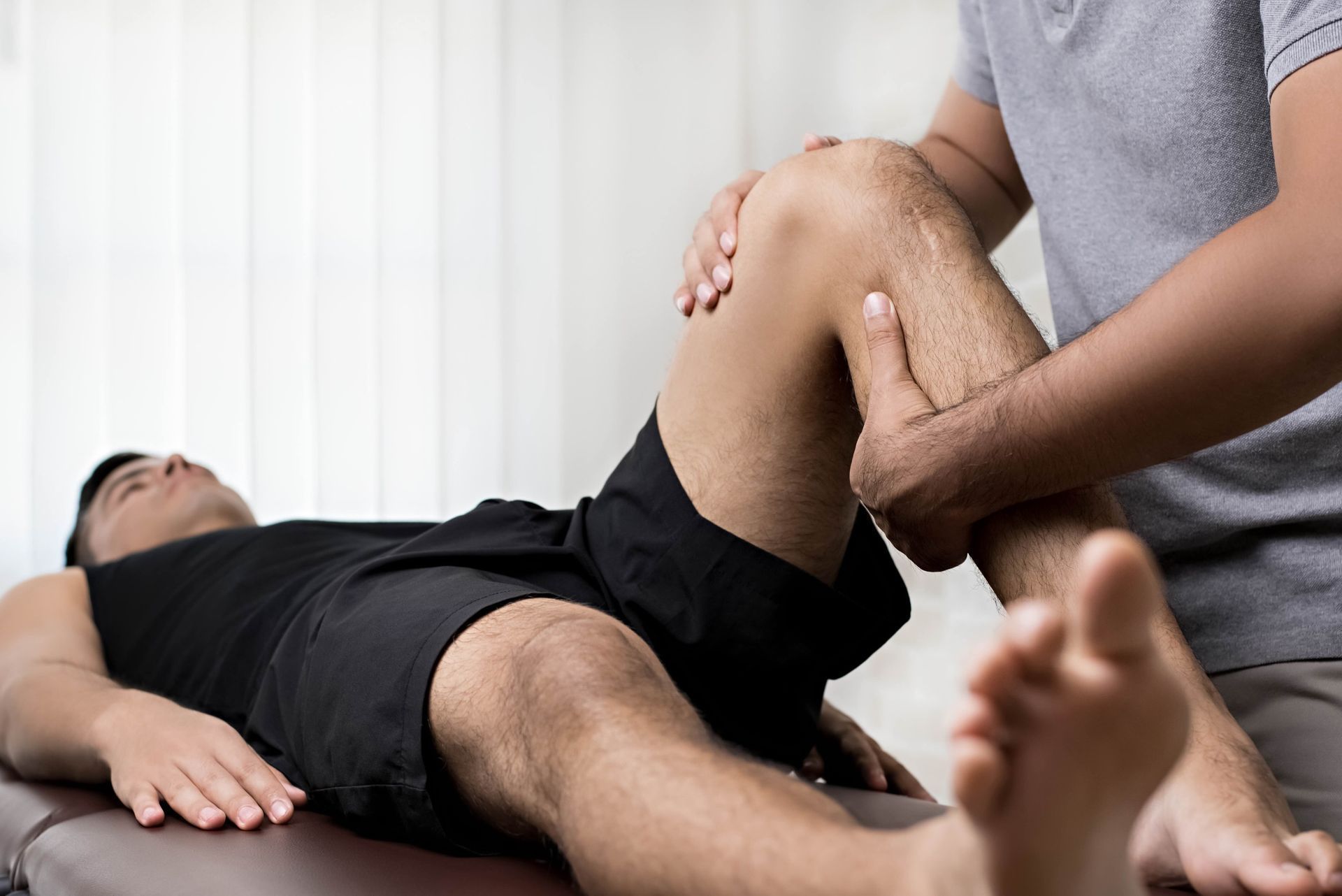 A man is laying on a table getting his knee examined by a doctor.