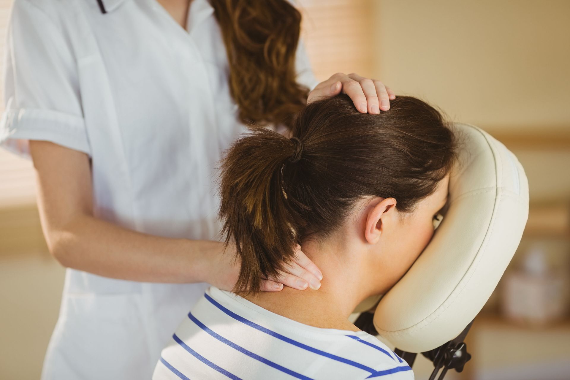 A woman is getting a massage on her neck in a chair.