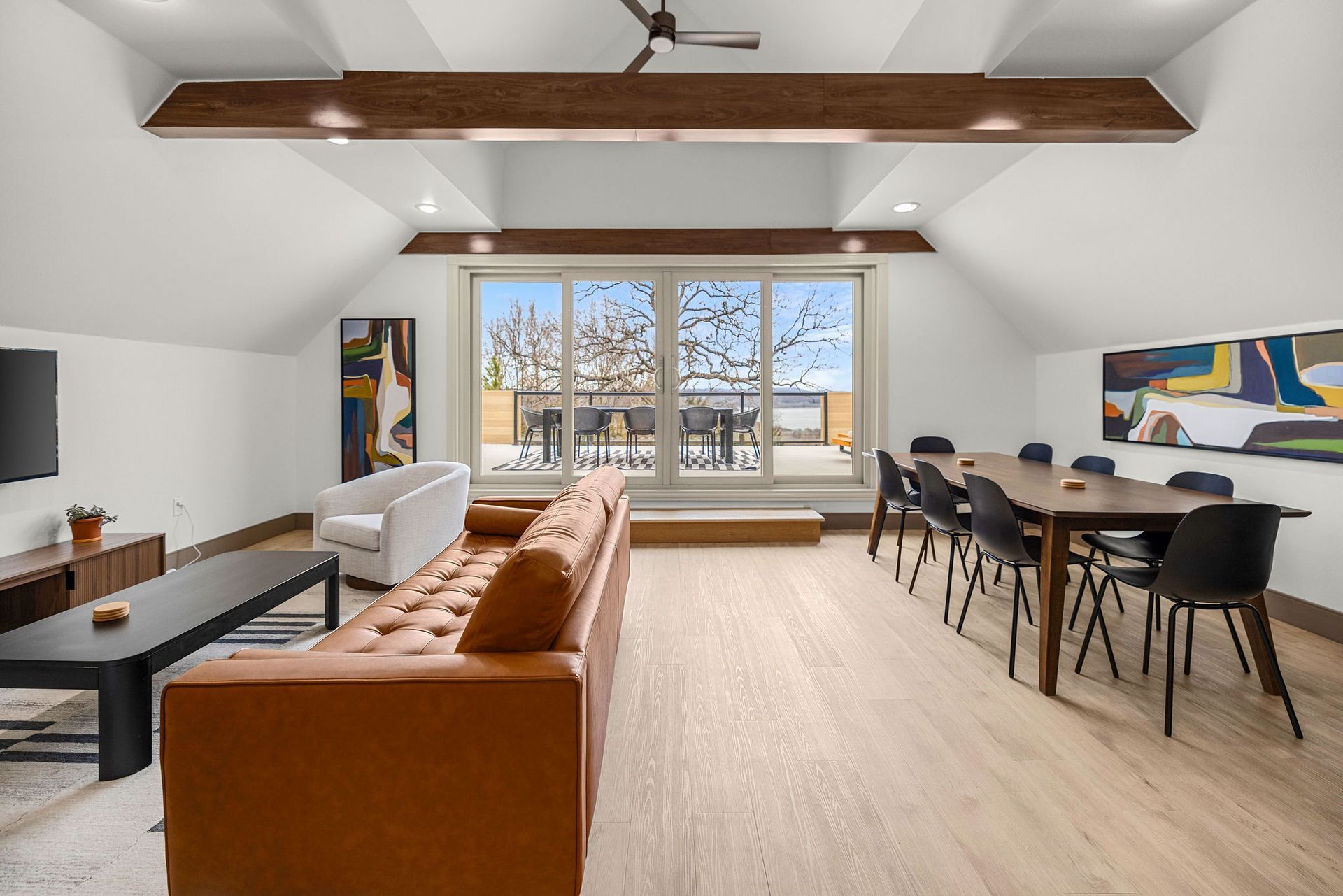 Spacious living area with tan leather sofa, dining table, and large sliding glass doors leading to a patio.