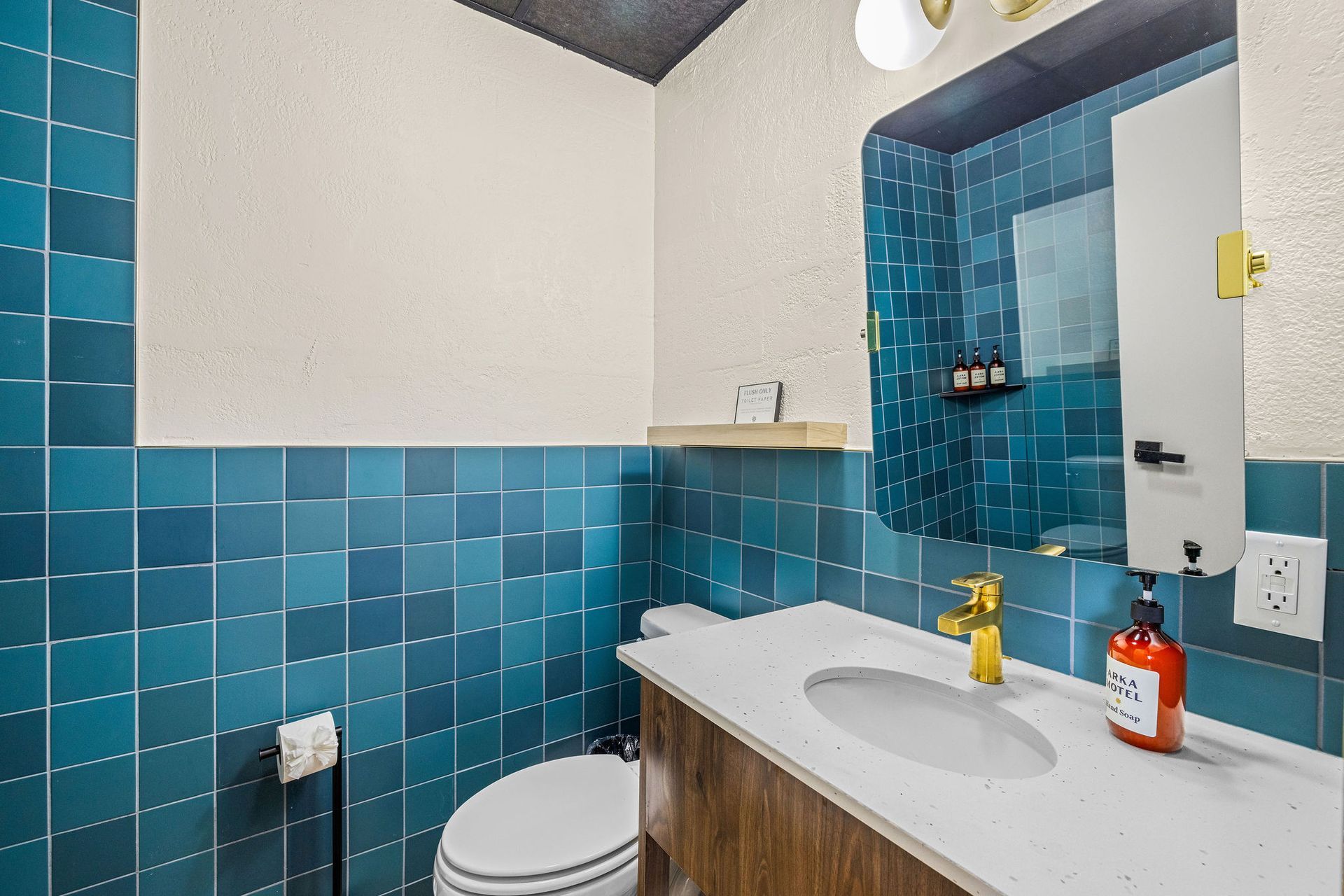 The bathroom with blue tile on the walls, a white toilet, and a wooden vanity.