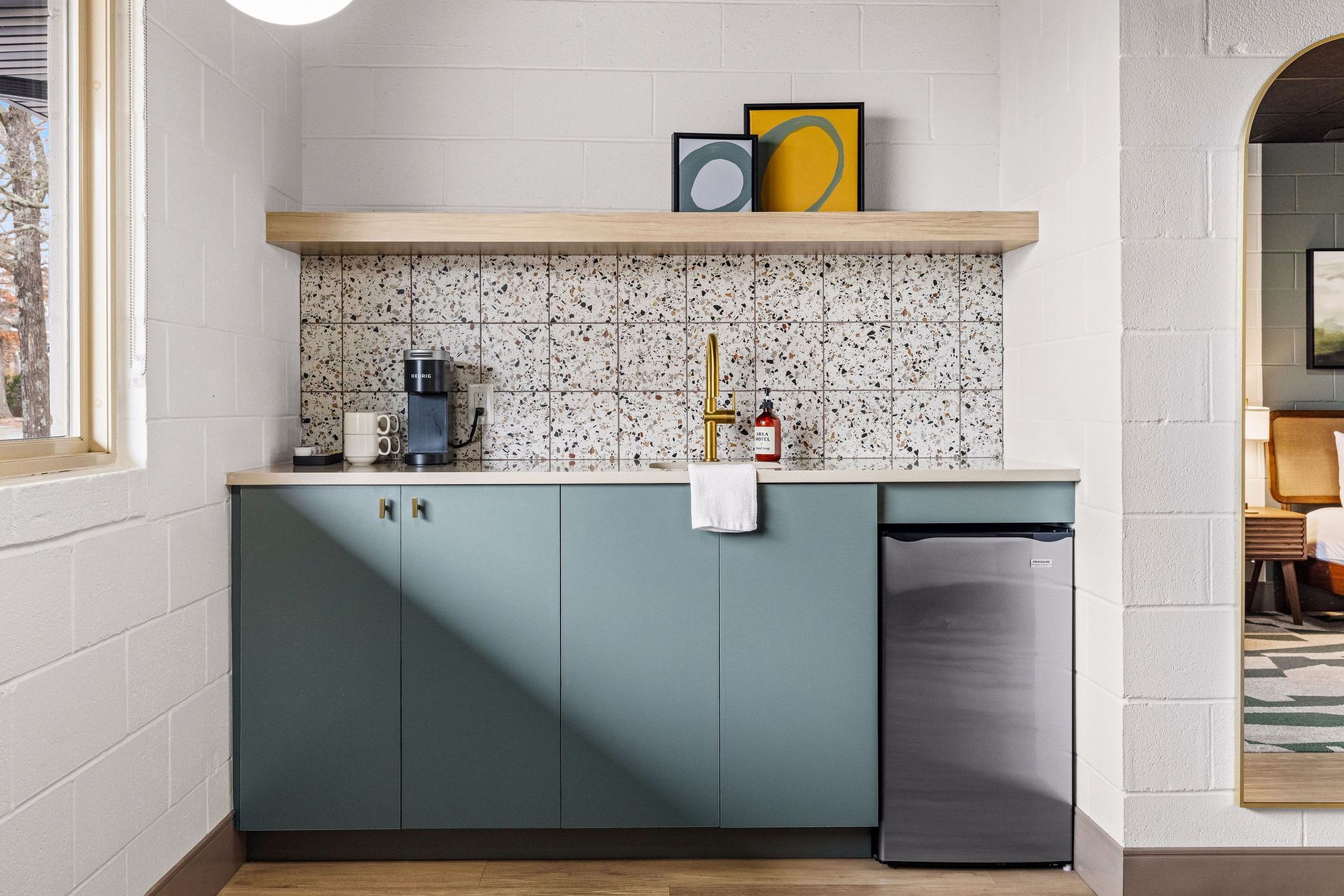 A small kitchenette with green cabinets, a mini fridge, and coffee maker.