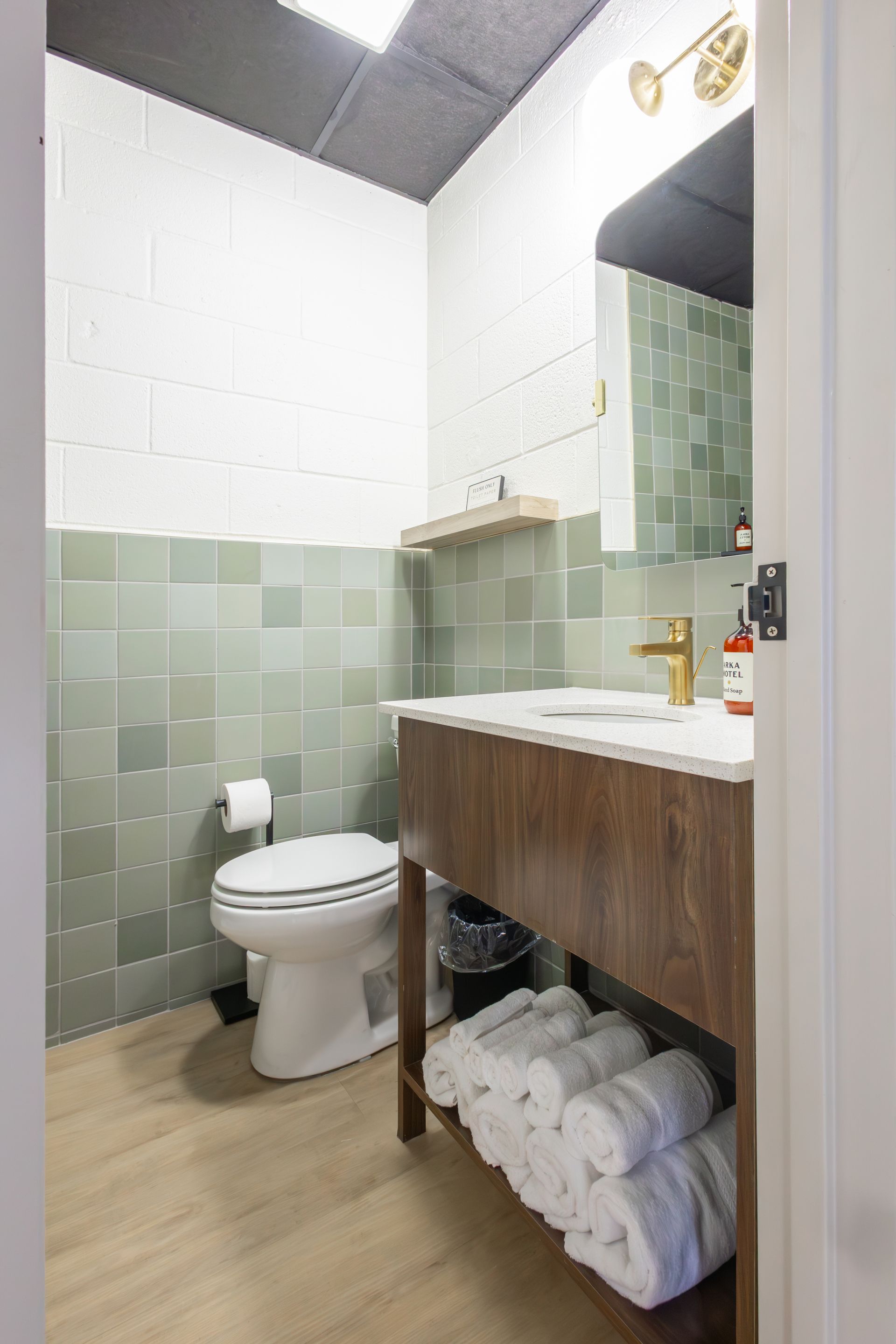 The bathroom with green tile and a small wooden vanity.