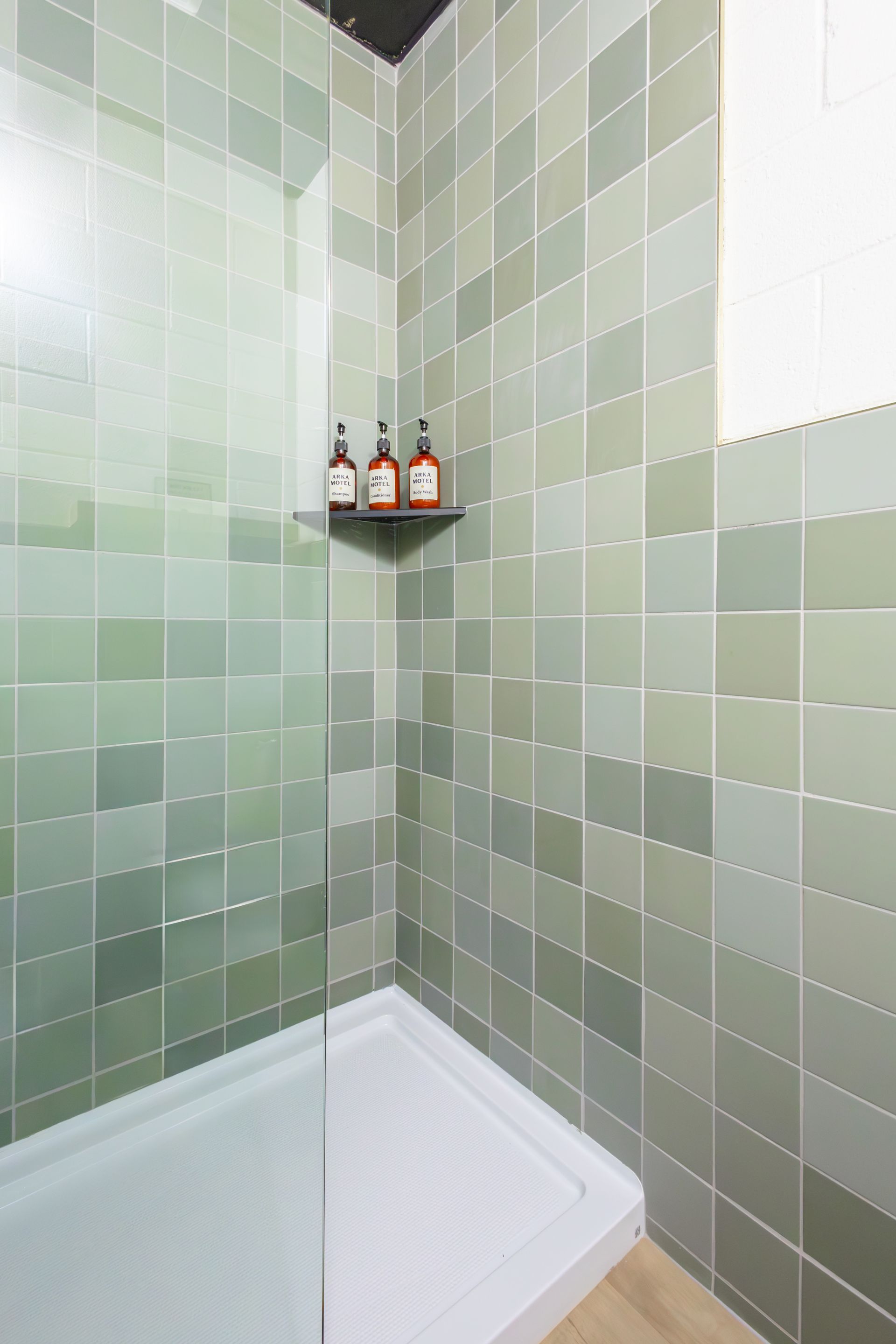 The shower with green tile and three shampoo bottles.