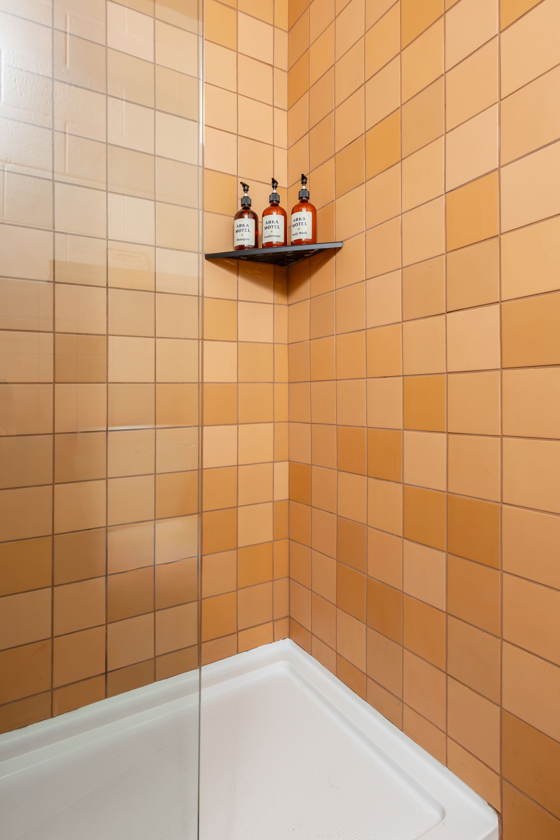 A bathroom with terracotta colored tile with shampoo bottles on a shelf.